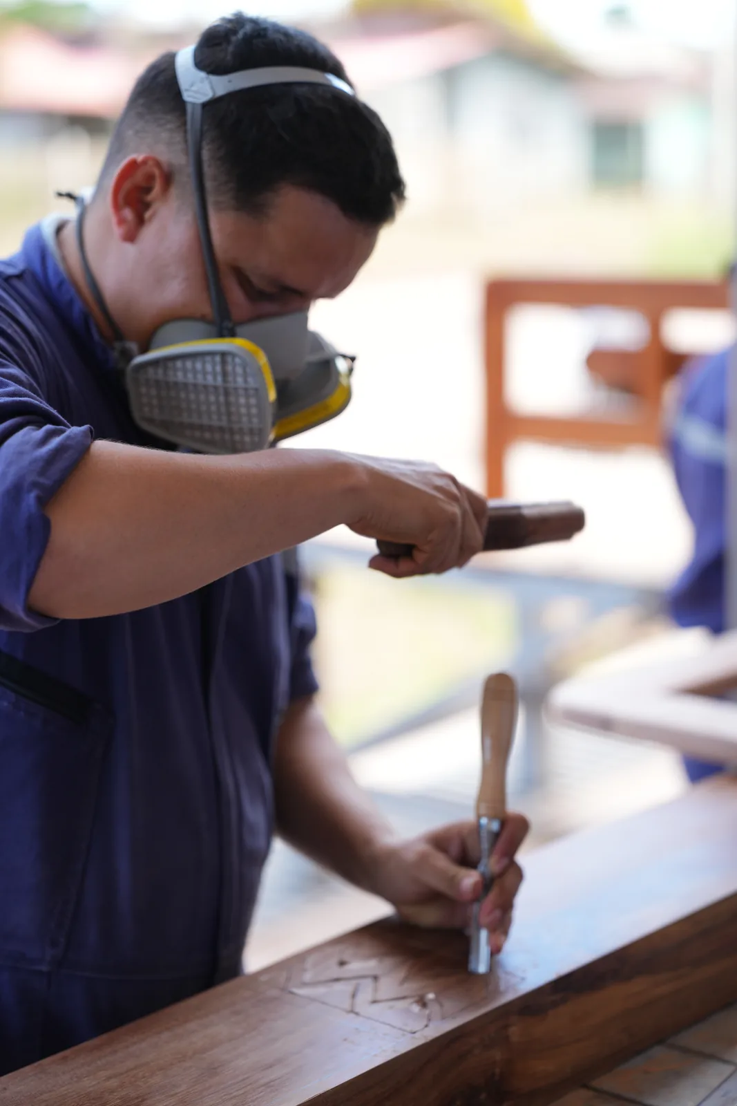 Ebanista golpea el formón con una maceta de madera para tallar un motivo decorativo en el travesaño de un cabecero